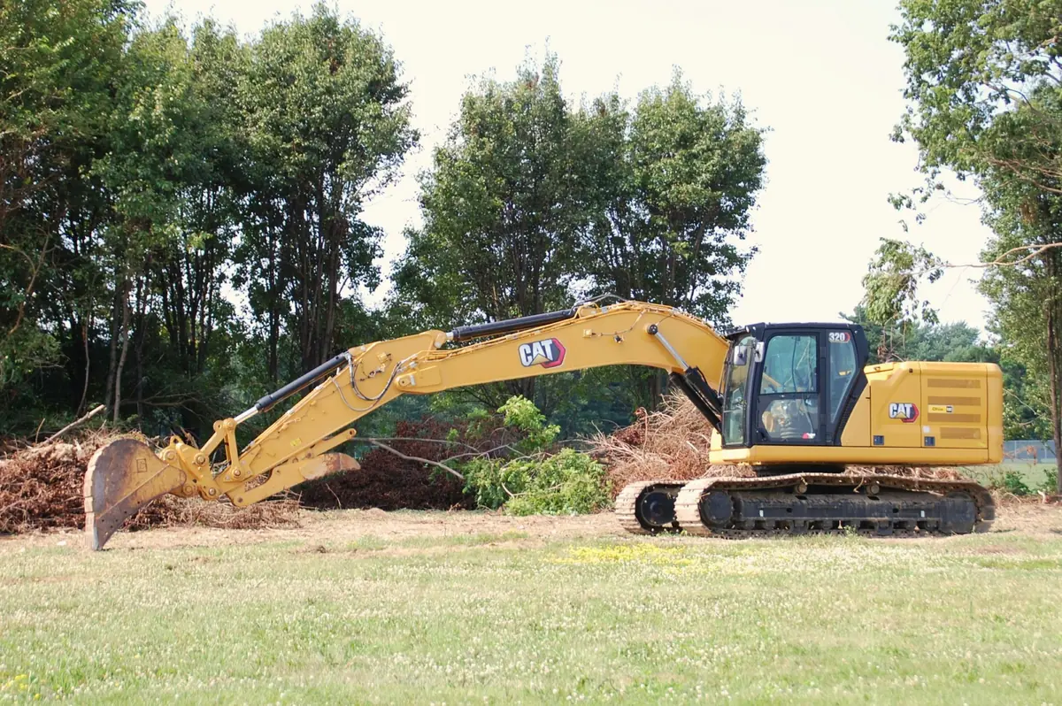 Bagger räumt Gehölz auf einer Wiesenfläche vor Baubeginn